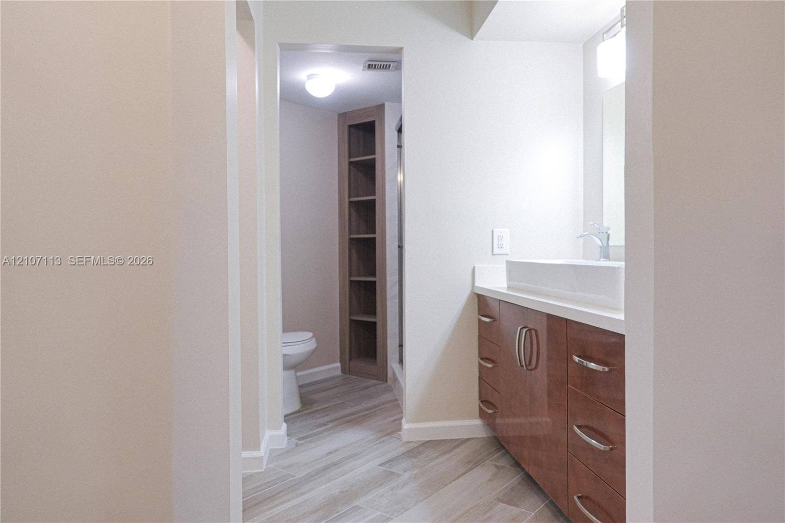 10451 W Broward Boulevard, #102, Plantation, Plantation, FL 33324 Bathroom featuring a vanity with high-gloss wood-finish cabinetry, a rectangular vessel sink, stone-composite countertop, wood-finish shelving, and wood-finish tile flooring