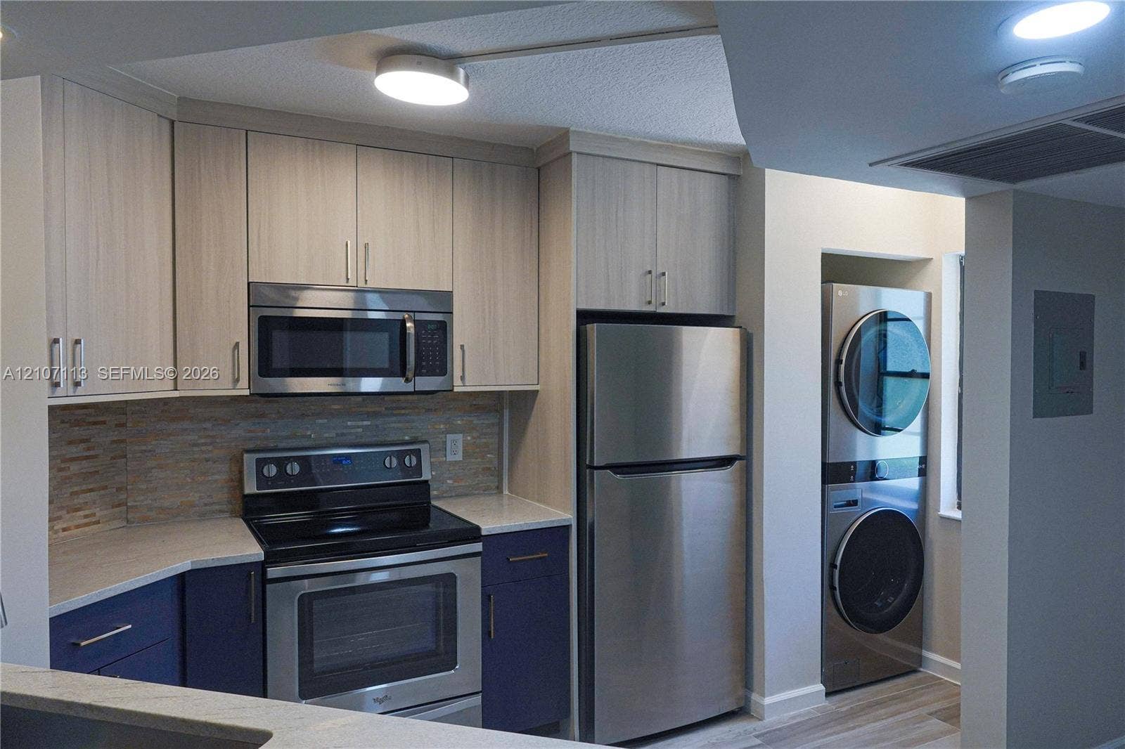 10451 W Broward Boulevard, #102, Plantation, Plantation, FL 33324 Kitchen featuring dual-toned cabinetry, light-toned countertops, a horizontal tile backsplash, stainless steel appliances, and an integrated stacked laundry unit