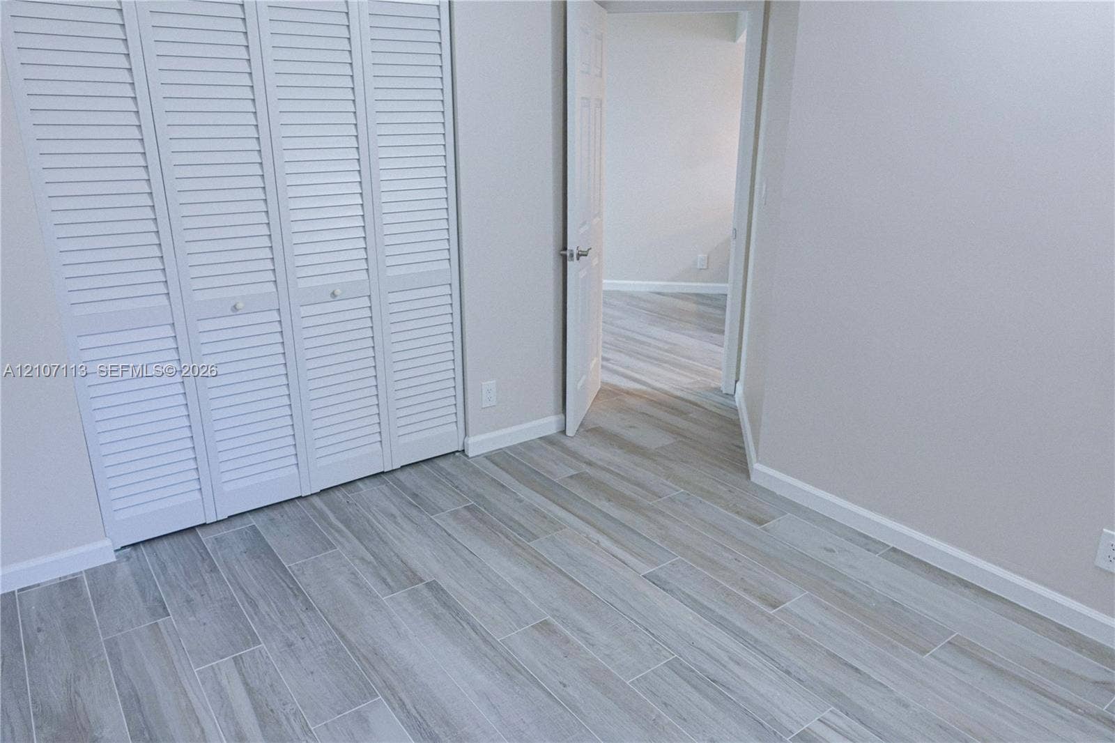 10451 W Broward Boulevard, #102, Plantation, Plantation, FL 33324 Wood-finish plank flooring featuring neutral grey tones, louvered bi-fold closet doors, and interior hinged door with brushed nickel hardware
