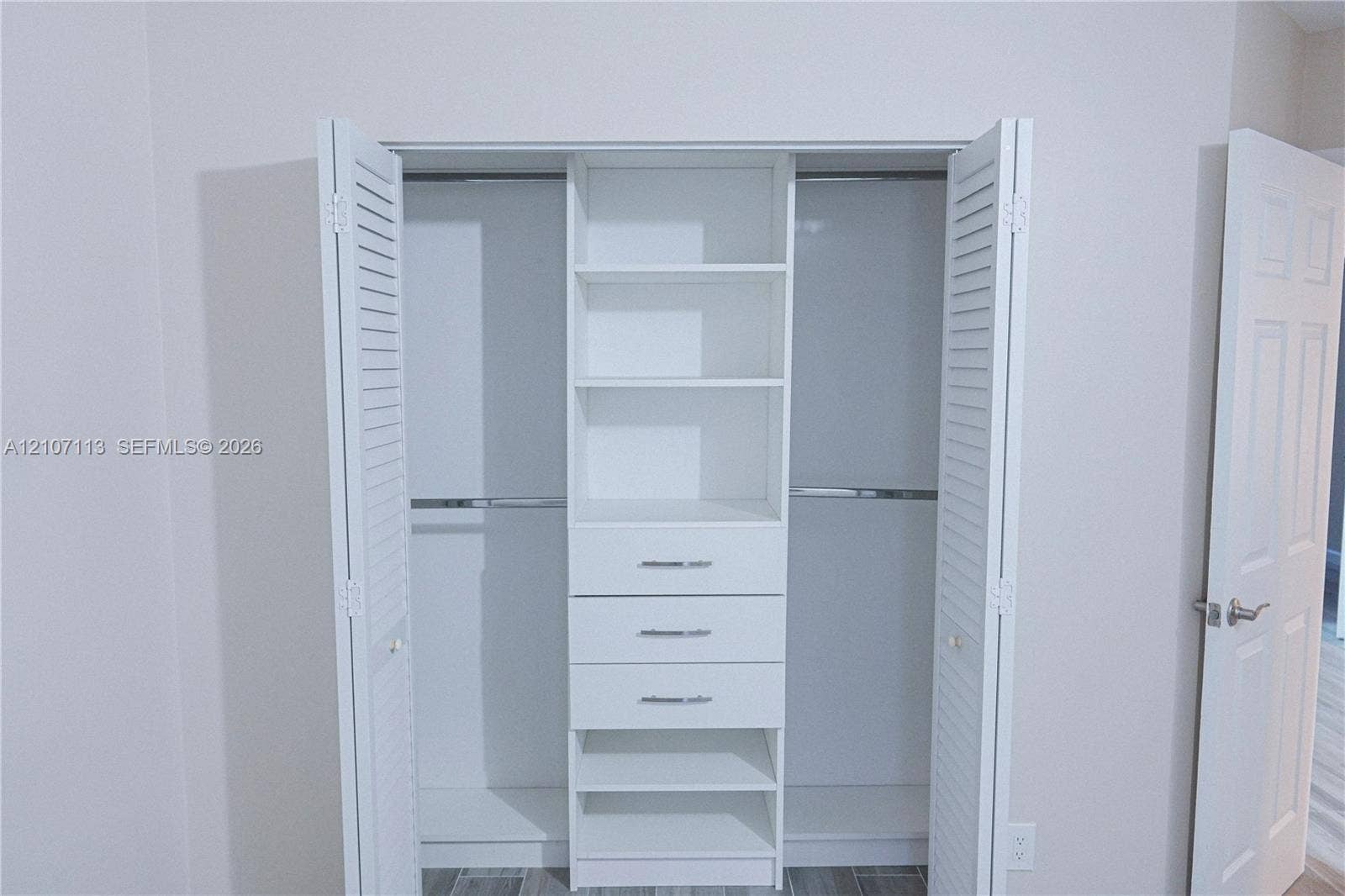 10451 W Broward Boulevard, #102, Plantation, Plantation, FL 33324 Closet featuring white louvered bifold doors, built-in shelving, three storage drawers with metallic hardware, and dual hanging rods