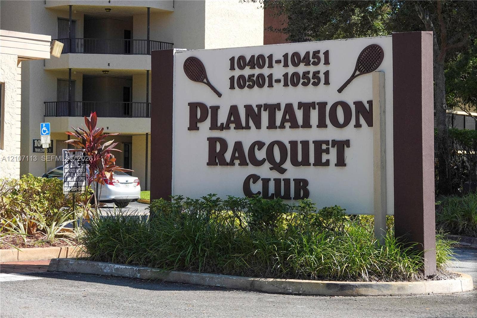 10451 W Broward Boulevard, #102, Plantation, Plantation, FL 33324 Plantation Racquet Club monument signage featuring dark brown lettering and structural pillars, set within a landscaped area with manicured shrubbery