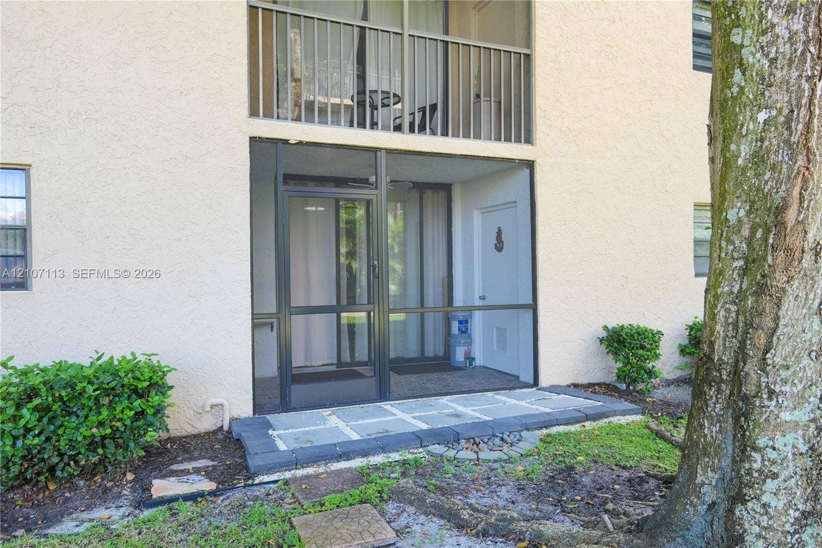10451 W Broward Boulevard, #102, Plantation, Plantation, FL 33324 Stucco exterior featuring a screened-in ground-level patio, a stone-paver walkway, and a second-story balcony with metal railings
