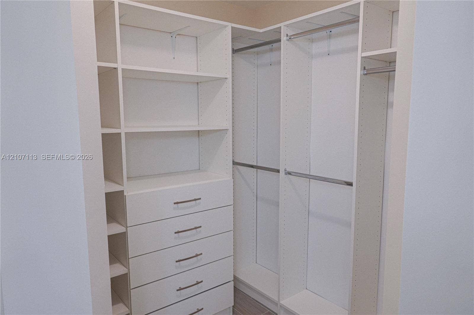 10451 W Broward Boulevard, #102, Plantation, Plantation, FL 33324 Built-in closet system featuring white modular cabinetry, adjustable shelving, integrated five-drawer dresser, and multiple stainless steel hanging rods