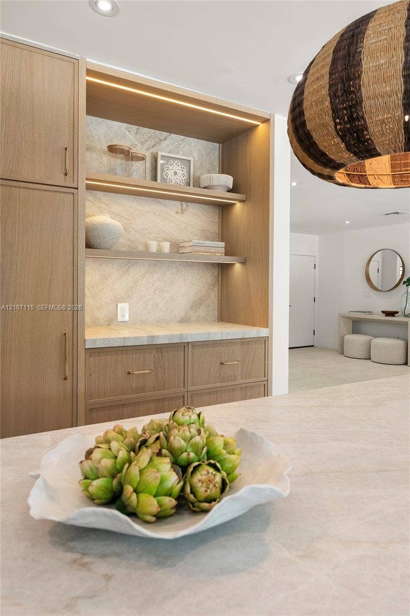 Built-in wood-finish cabinetry featuring integrated recessed lighting, stone-surface countertop, open shelving, and brushed brass hardware
