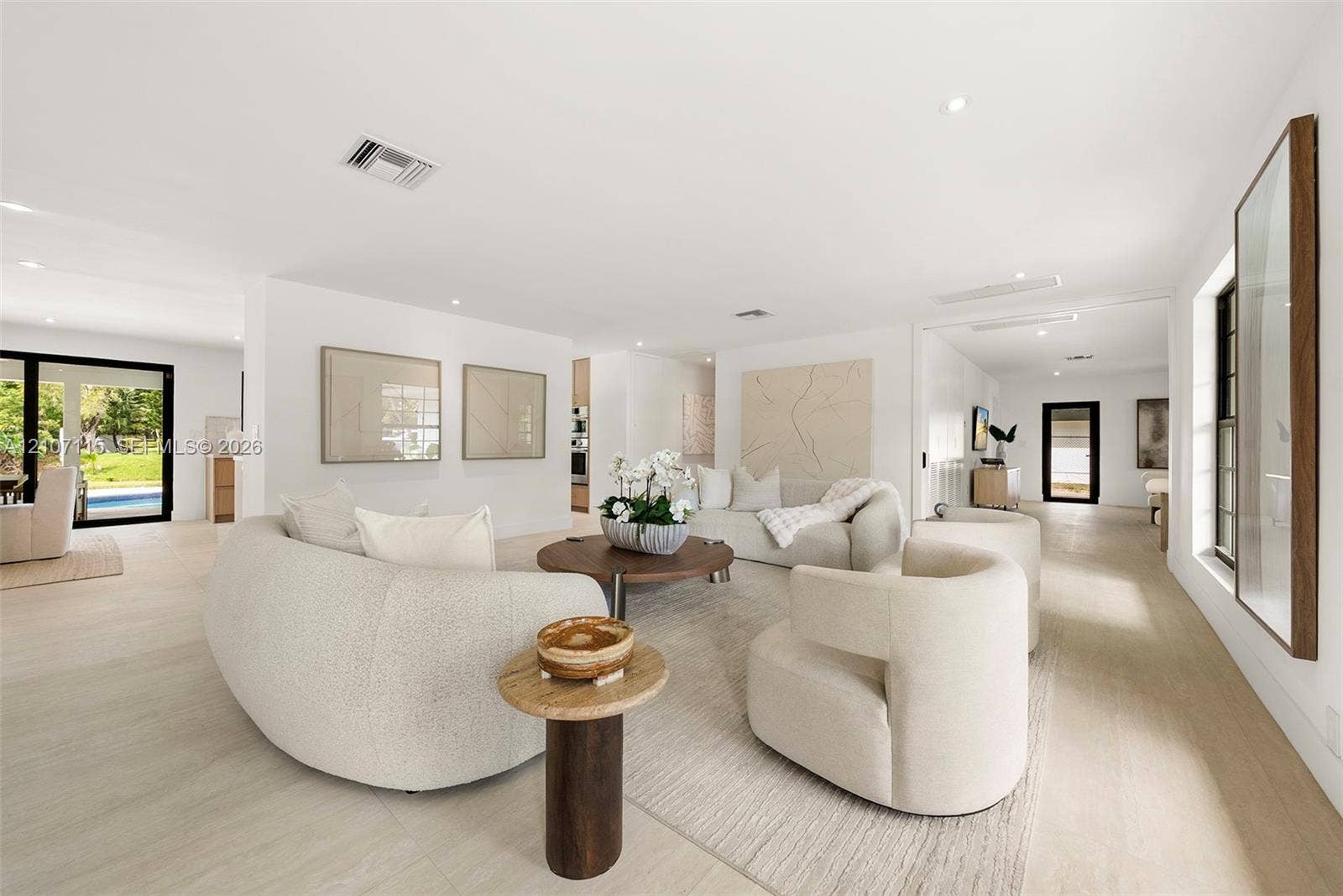 Open-concept interior featuring light-toned wood-finish flooring, recessed lighting, and expansive glass doors