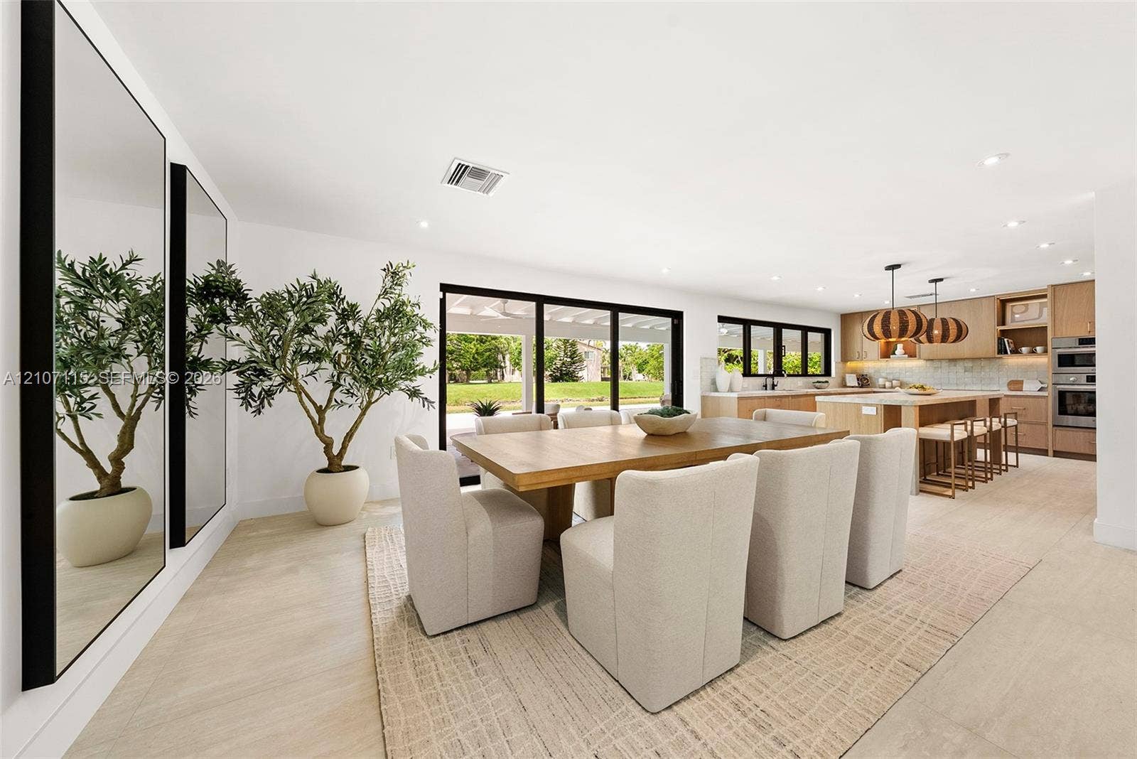 Open-concept interior featuring light-toned tile flooring, custom wood cabinetry, a built-in double wall oven, and sliding multi-panel glass doors