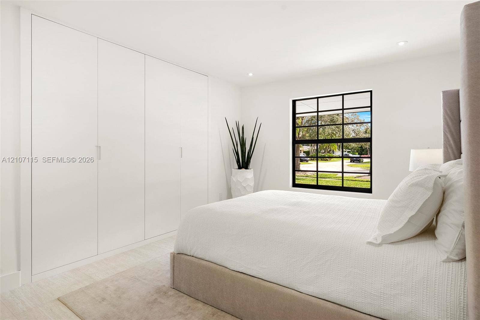 Bedroom 3 Full-wall built-in cabinetry with flush-panel doors, grid-pattern window with matte black frame, recessed ceiling lighting, and neutral stone-finish flooring