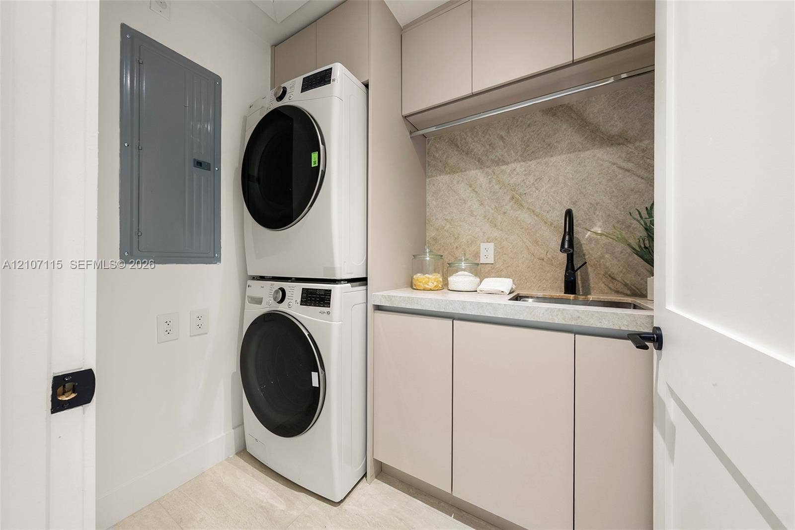 Laundry area featuring floor-to-ceiling built-in cabinetry, a stone-finish backsplash, undermount sink with a matte black faucet, and stone-surface countertop