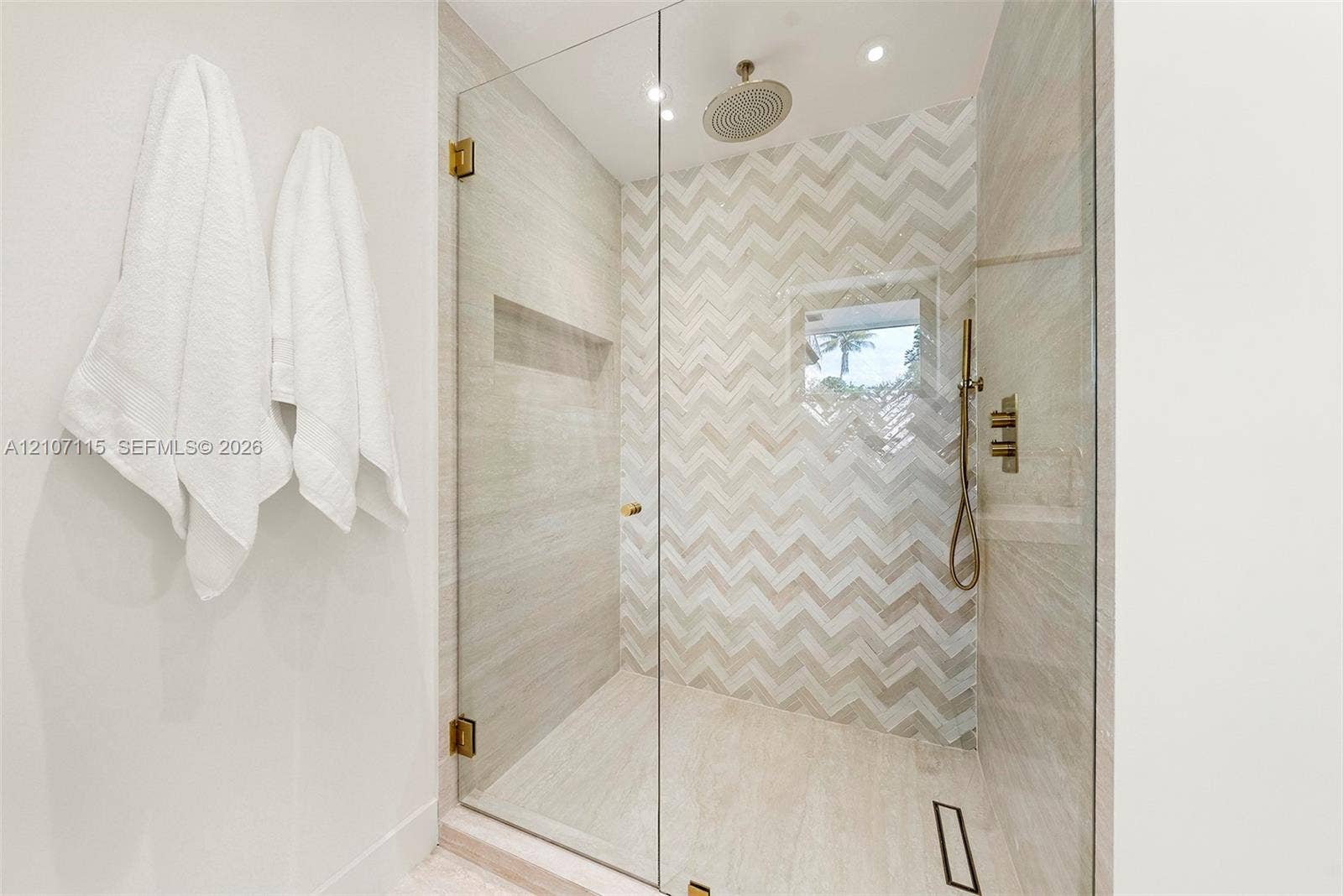 Walk-in shower featuring a chevron-patterned tile accent wall, glass enclosure, recessed wall niche, rainfall showerhead, and a handheld fixture