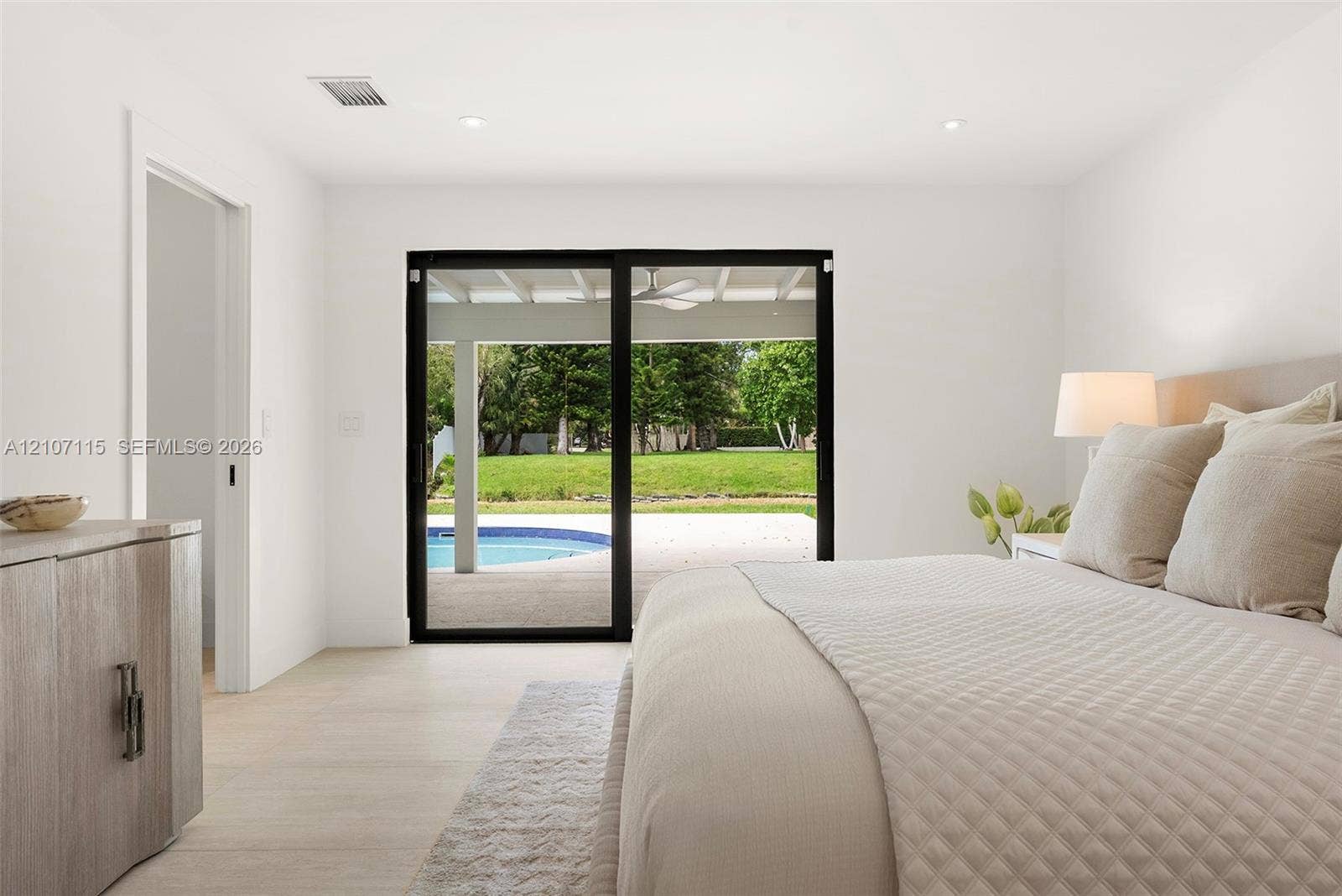 Light-filled interior featuring sliding glass doors with black frames, neutral stone-finish flooring, and recessed lighting