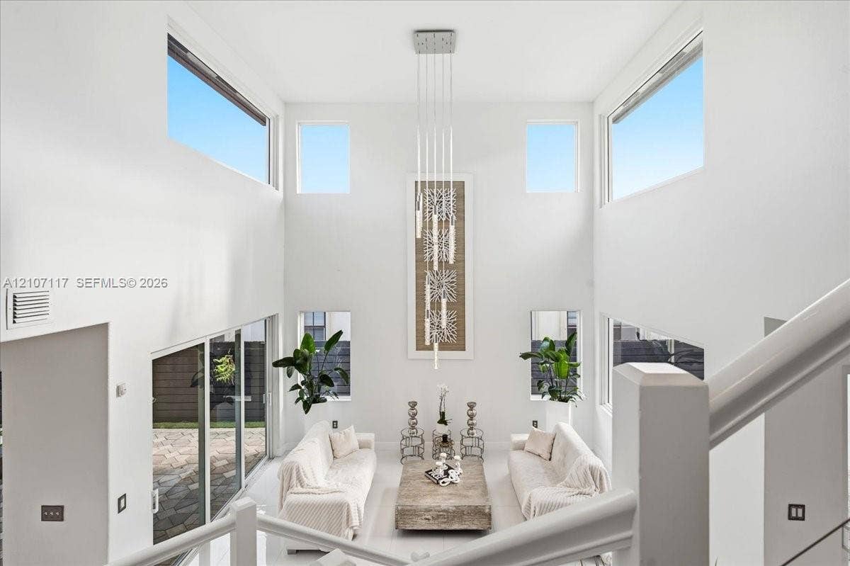 7863 NW 111th Court, Doral, FL 33178 Double-height ceilings, expansive window configuration, multi-level glass slider access to exterior patio, and tiered contemporary pendant lighting