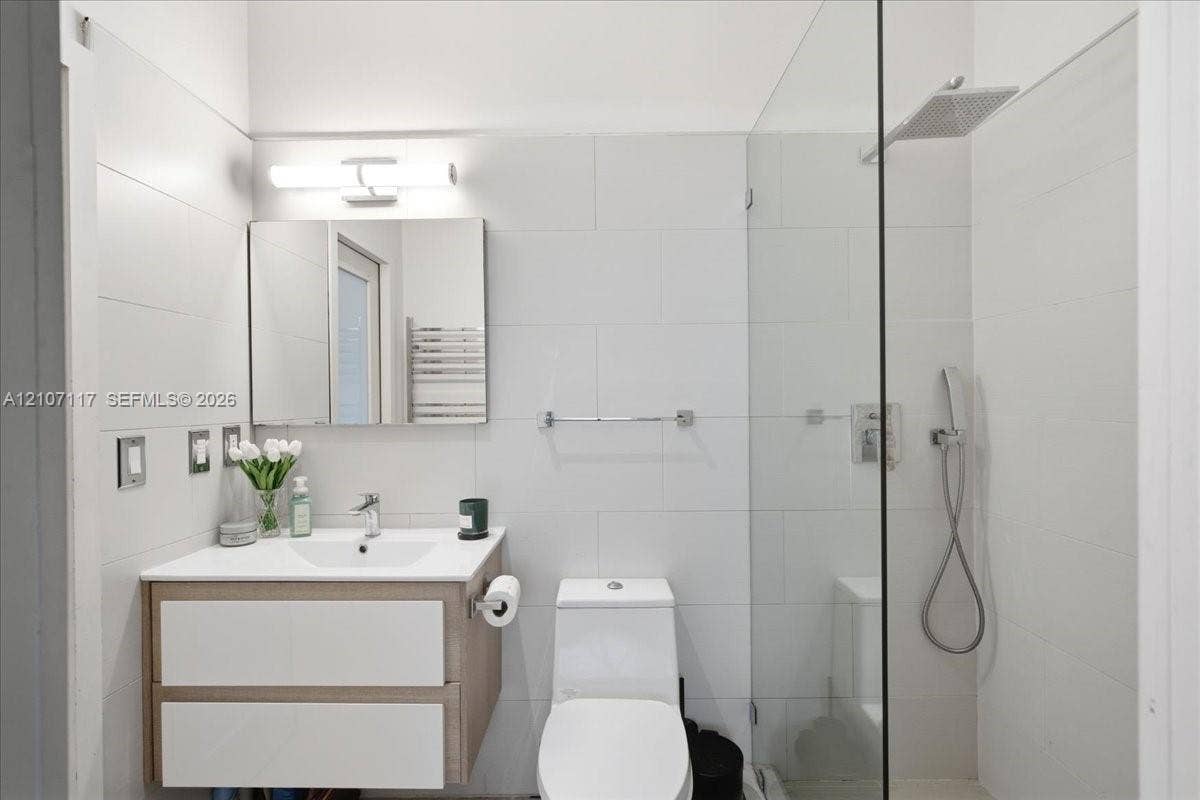 7863 NW 111th Court, Doral, FL 33178 Floating wood-finish vanity with a white countertop, walk-in shower with a glass panel, rainfall shower head, handheld sprayer, and wall-mounted vanity lighting