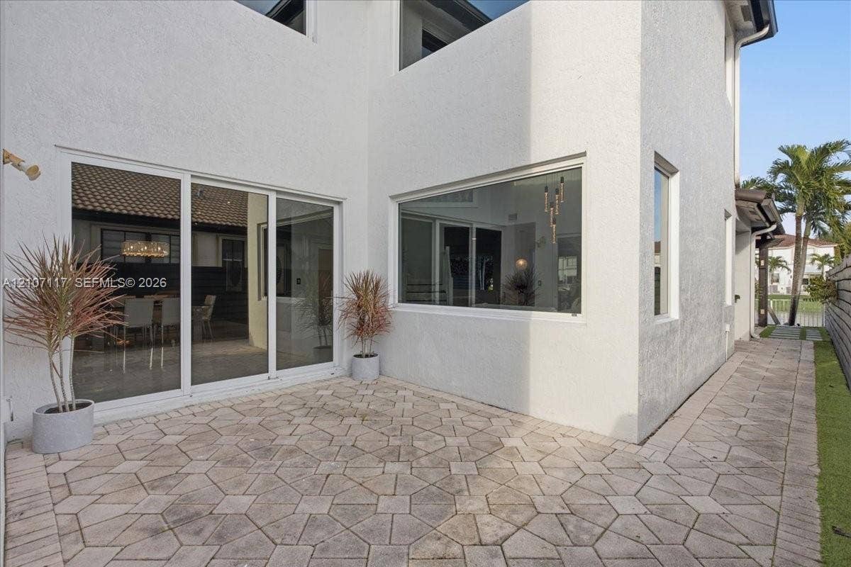 7863 NW 111th Court, Doral, FL 33178 Exterior patio featuring geometric stone pavers, white stucco facade, expansive sliding glass door system, and large rectangular fixed-pane windows