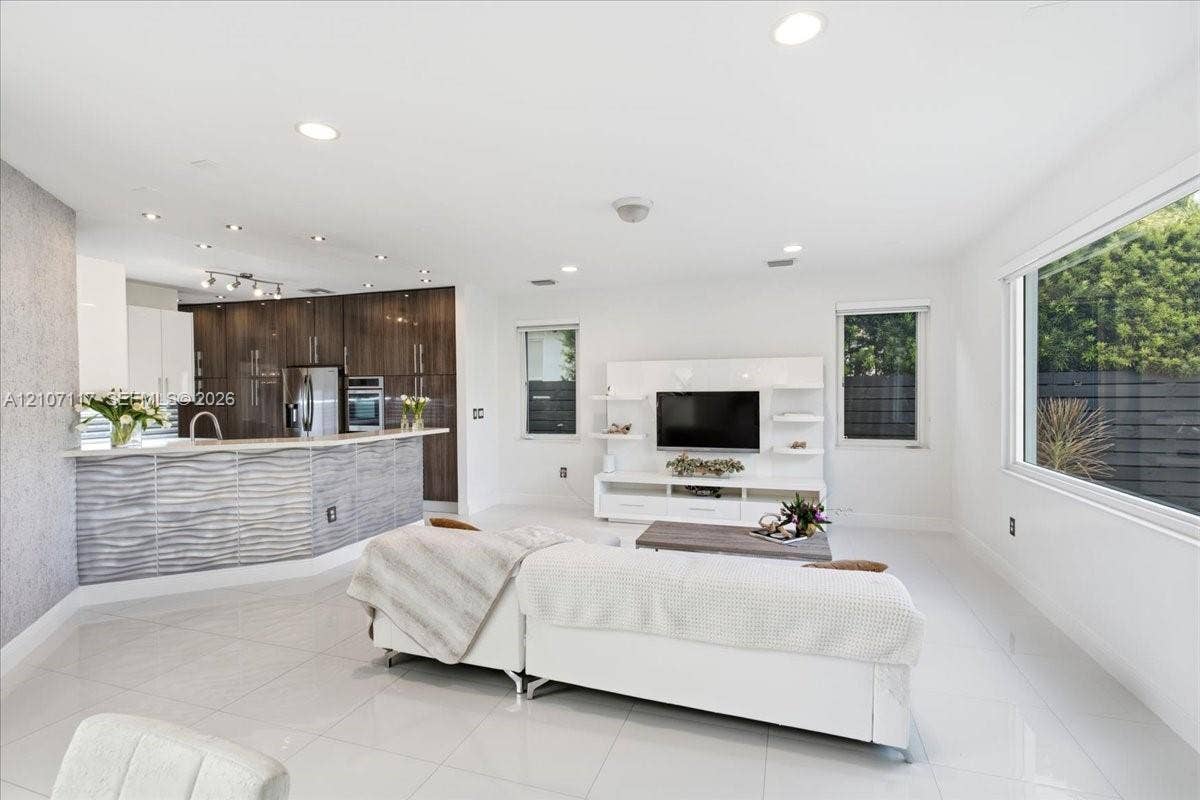 7863 NW 111th Court, Doral, FL 33178 Open-concept interior featuring large-format tile flooring, recessed lighting, and a kitchen island with a textured, wave-patterned facade