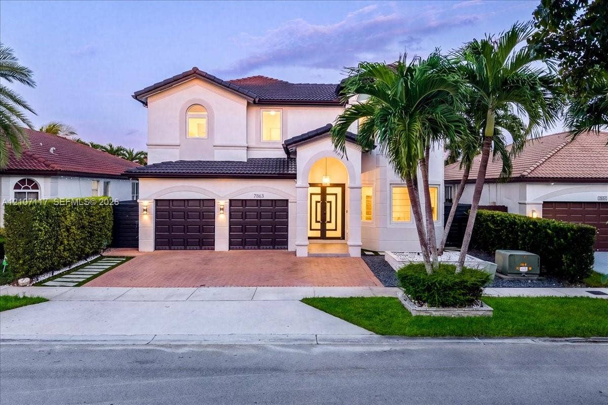 7863 NW 111th Court, Doral, FL 33178 Two-story stucco exterior featuring a tiled roof, arched entryway, brick-paver driveway, double garage, and geometric-patterned glass front door