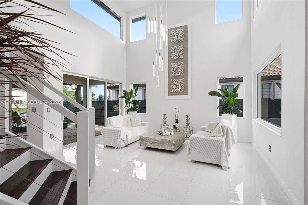 7863 NW 111th Court, Doral, FL 33178 Double-height ceilings featuring tiered modern pendant lighting and multi-level windows, polished porcelain tile flooring, and a staircase with wood-finish treads and cable railing