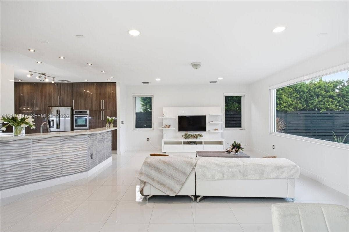 7863 NW 111th Court, Doral, FL 33178 Open-concept interior featuring large-format tile flooring, recessed ceiling lighting, kitchen cabinetry with a horizontal wood-grain finish, and a peninsula with a textured, undulating gray facade