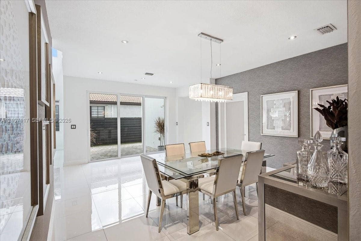 7863 NW 111th Court, Doral, FL 33178 Dining area featuring polished large-format tile flooring, a rectangular multi-light glass pendant fixture, textured grey accent wall, and sliding glass doors