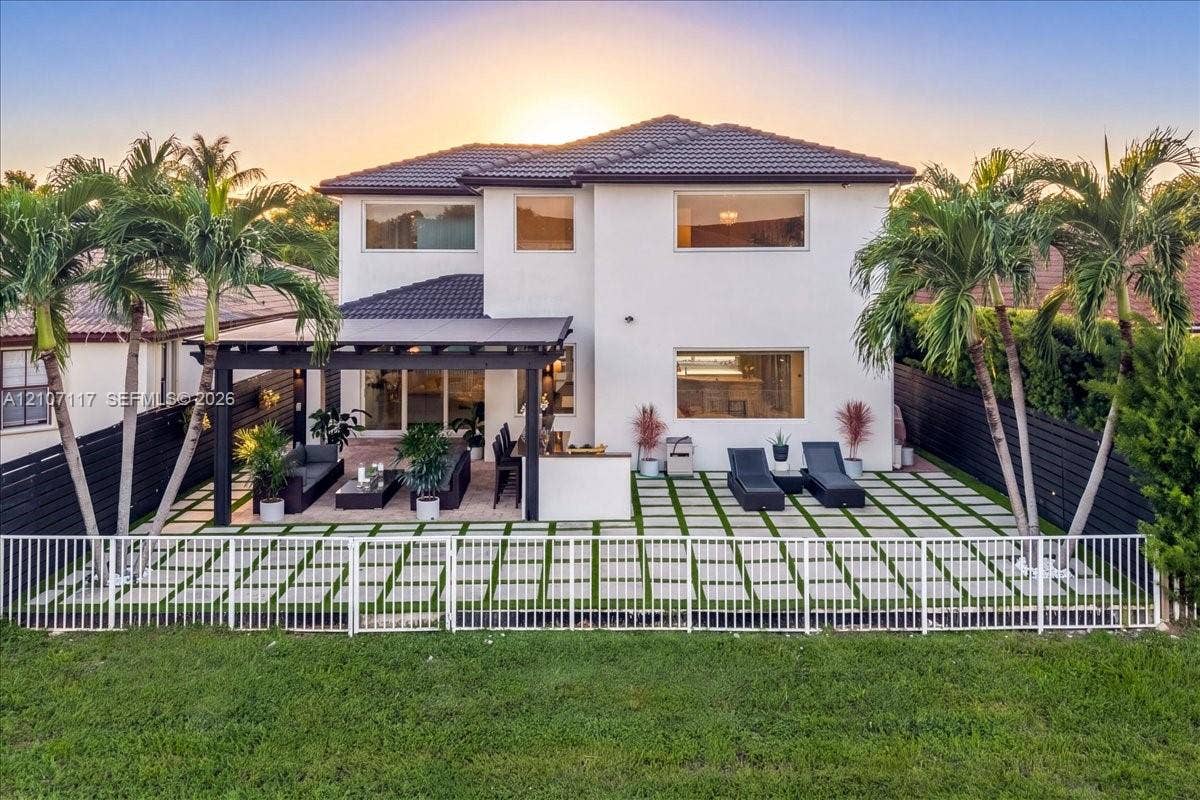 7863 NW 111th Court, Doral, FL 33178 Two-story residence featuring a tile roof, an expansive paver patio with grass inserts, a covered pergola, and a white aluminum perimeter fence