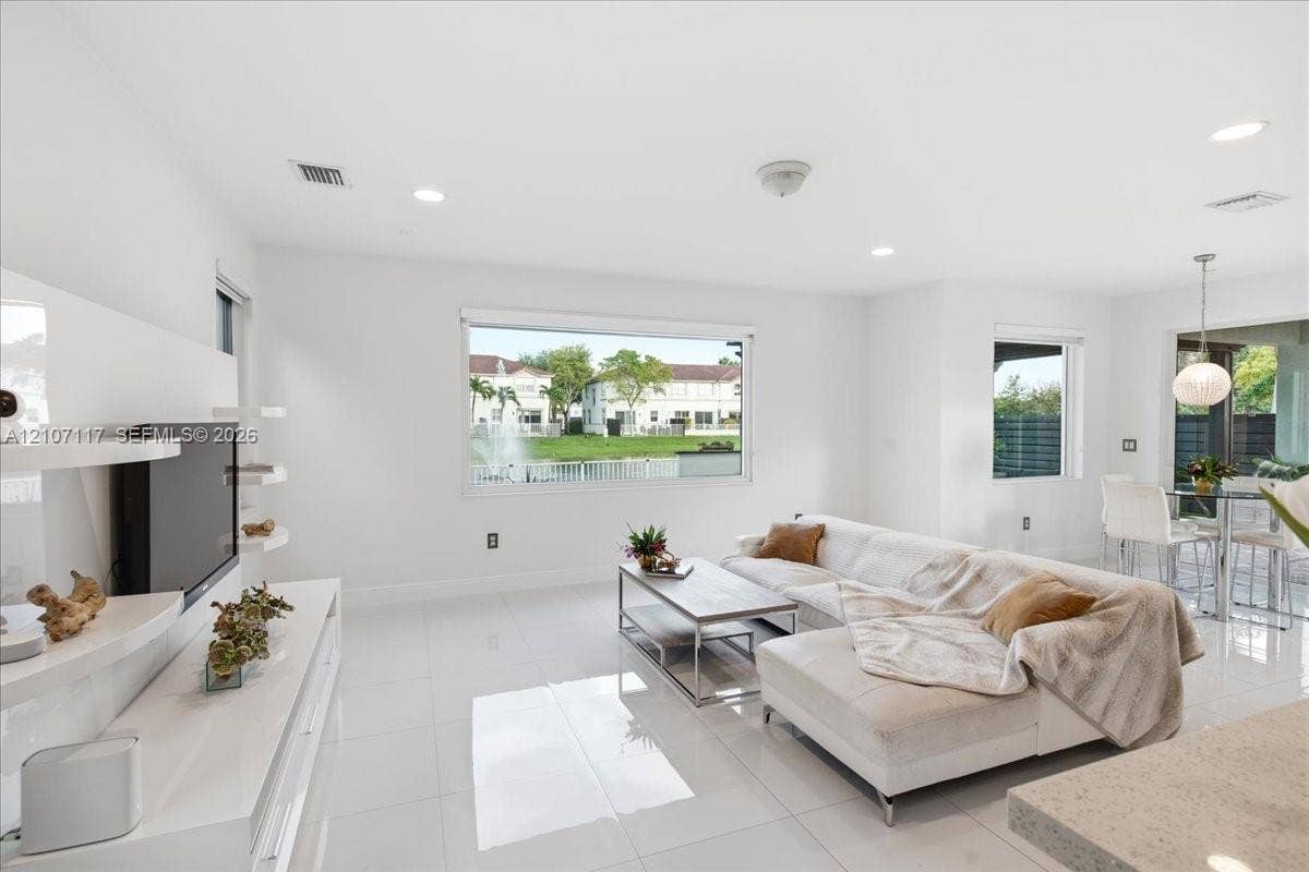 7863 NW 111th Court, Doral, FL 33178 Open-concept living space featuring high-gloss tile flooring, recessed lighting, built-in media shelving, and large windows with water exposure