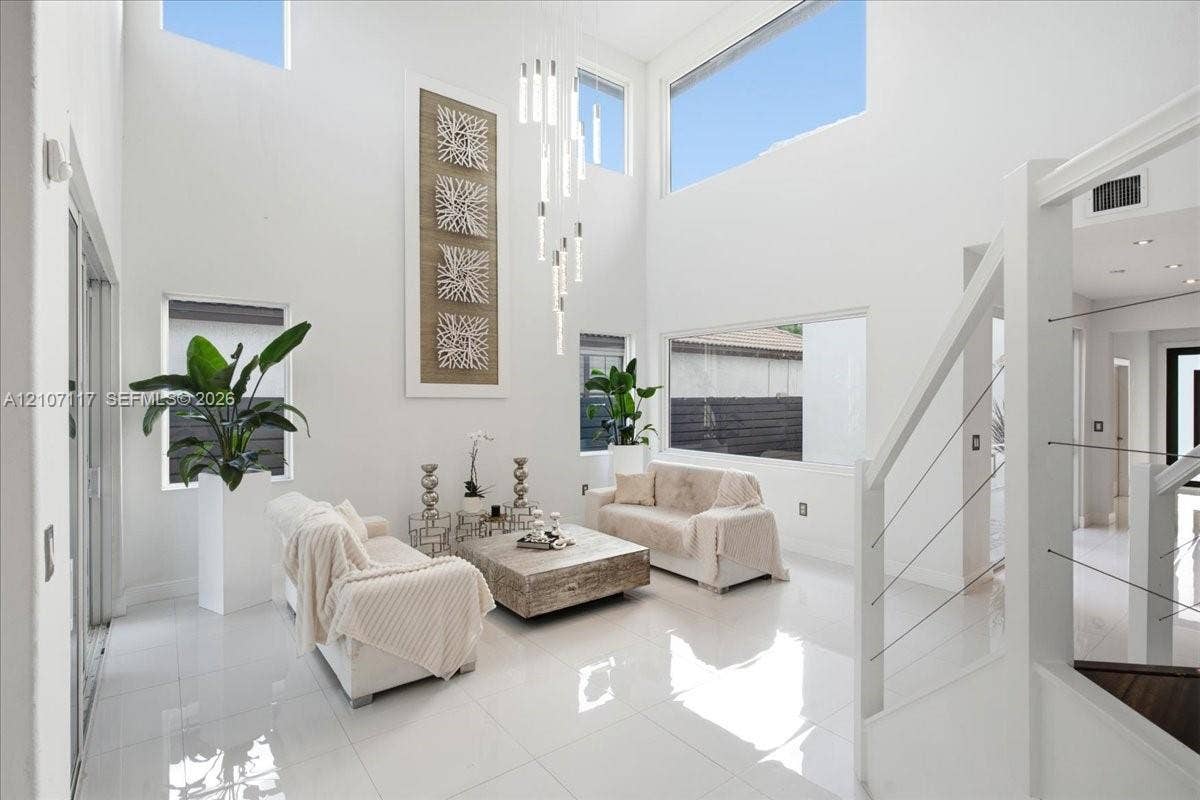 7863 NW 111th Court, Doral, FL 33178 Double-height living area featuring floor-to-ceiling windows, polished tile flooring, contemporary multi-pendant lighting, and a staircase with stainless steel cable railing