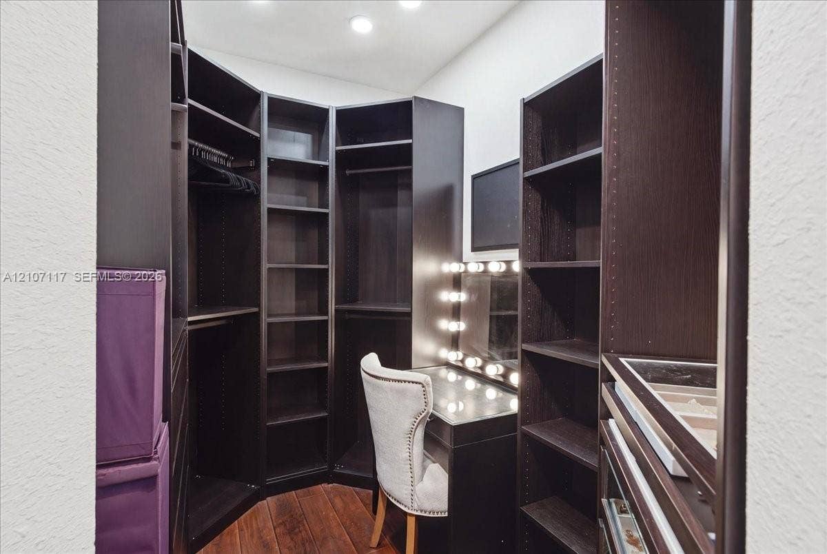 7863 NW 111th Court, Doral, FL 33178 Walk-in closet featuring dark-finish custom built-in cabinetry, floor-to-ceiling shelving, integrated vanity lighting, and wood-finish flooring