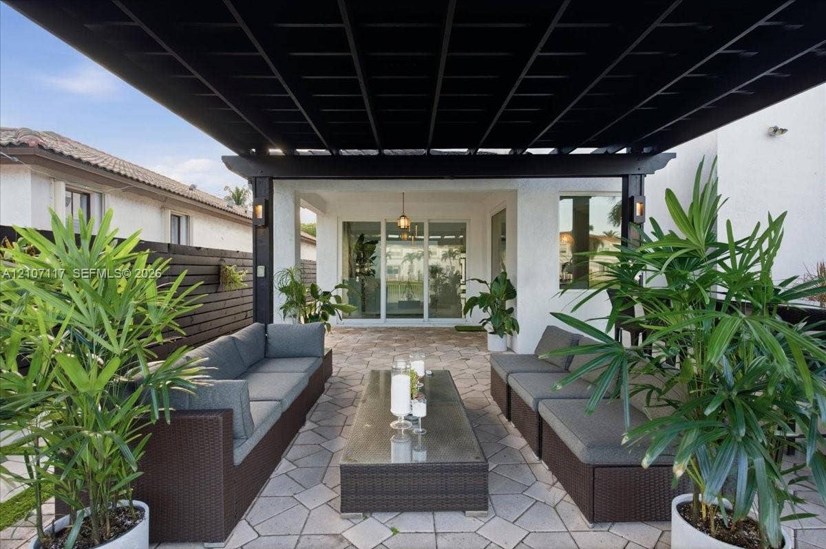 7863 NW 111th Court, Doral, FL 33178 Outdoor patio featuring a black timber pergola, paved stone flooring, horizontal privacy fencing, and recessed exterior wall lighting