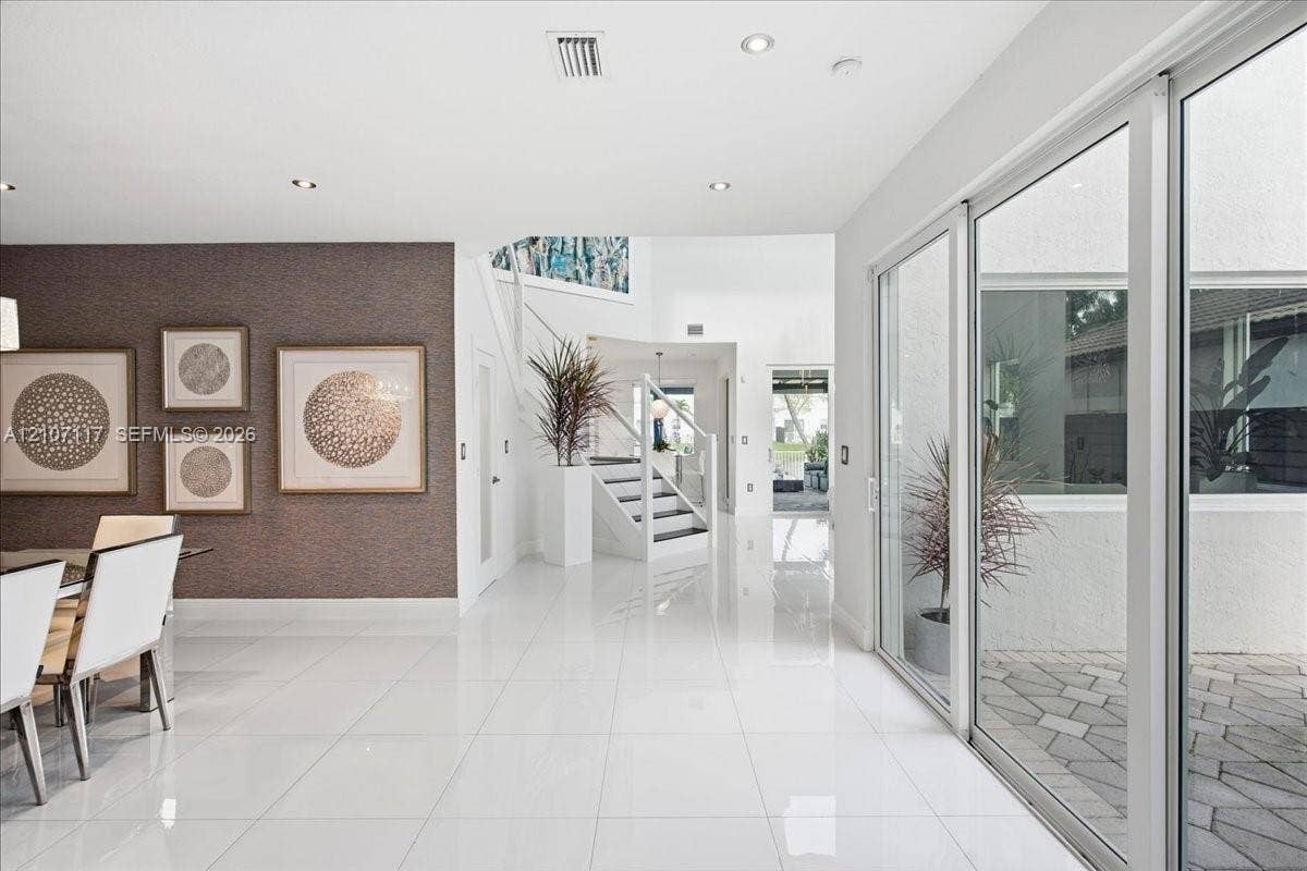 7863 NW 111th Court, Doral, FL 33178 Polished tile flooring, textured accent wall, staircase with glass panel railing, and expansive sliding glass doors