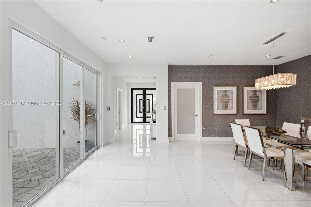 7863 NW 111th Court, Doral, FL 33178 Large-format white tile flooring, floor-to-ceiling glass sliding doors, recessed lighting, textured accent wall, and geometric-patterned entry door