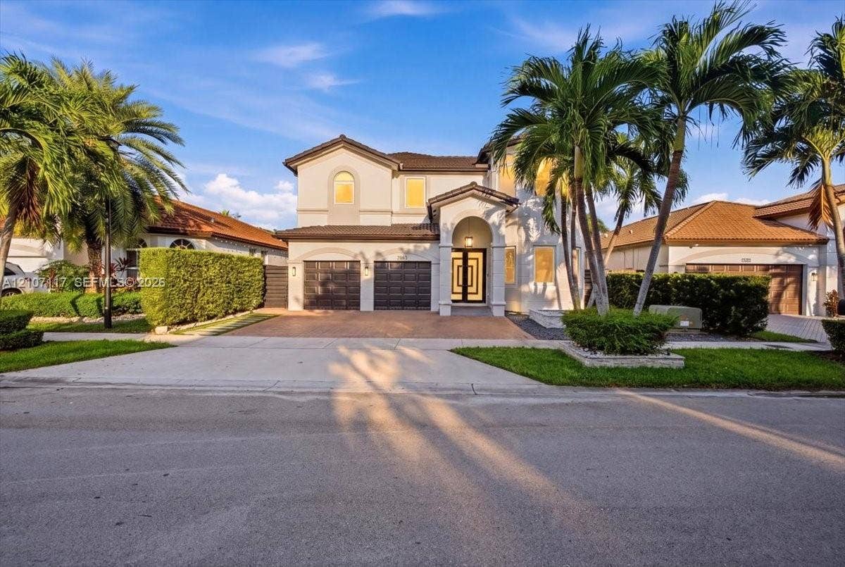 7863 NW 111th Court, Doral, FL 33178 Two-story residence featuring a tile roof, stucco exterior, covered entryway, and three-car garage with paneled doors