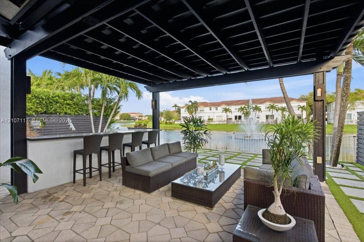 7863 NW 111th Court, Doral, FL 33178 Covered patio featuring a black pergola, stone paver flooring, and a built-in outdoor bar with a stone countertop