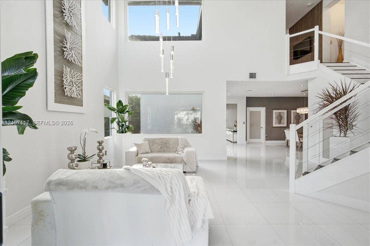 7863 NW 111th Court, Doral, FL 33178 Double-height ceiling, large-format polished tile flooring, staircase with cable railing, tiered contemporary chandelier, and expansive picture windows