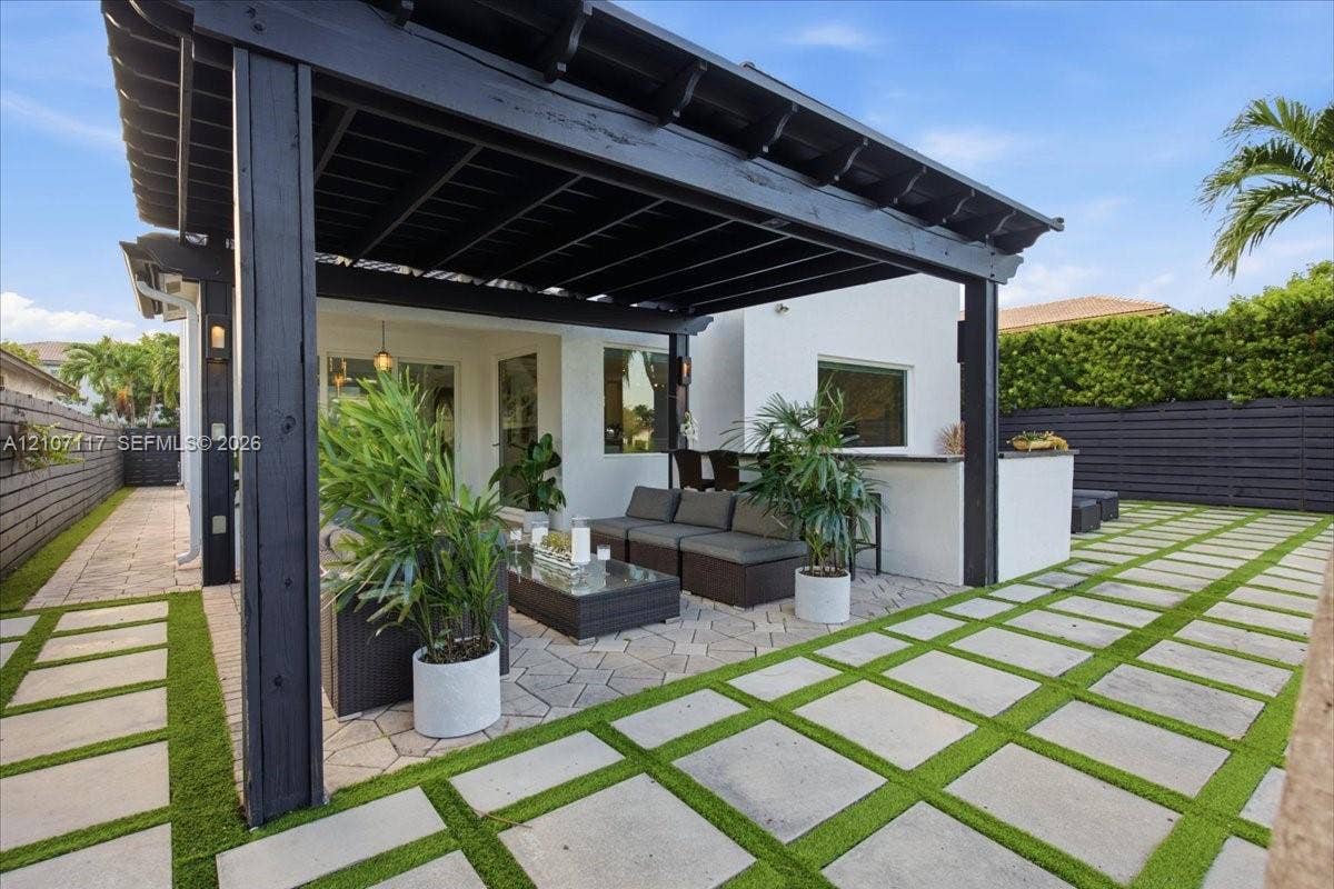 7863 NW 111th Court, Doral, FL 33178 Outdoor patio featuring a black timber pergola, built-in stone counter, and stone paver flooring with synthetic turf inlays