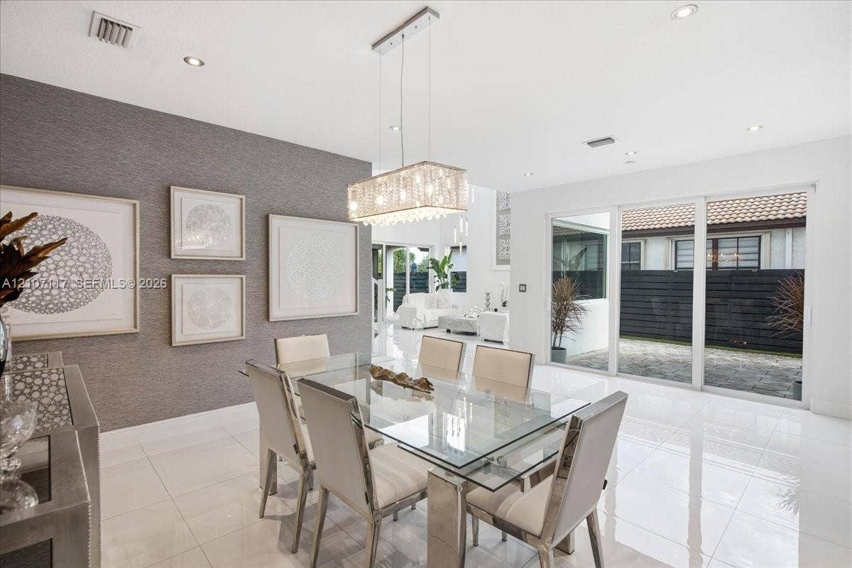 7863 NW 111th Court, Doral, FL 33178 Dining area featuring large-format tile flooring, textured accent wall, rectangular tiered crystal chandelier, and oversized glass sliding doors