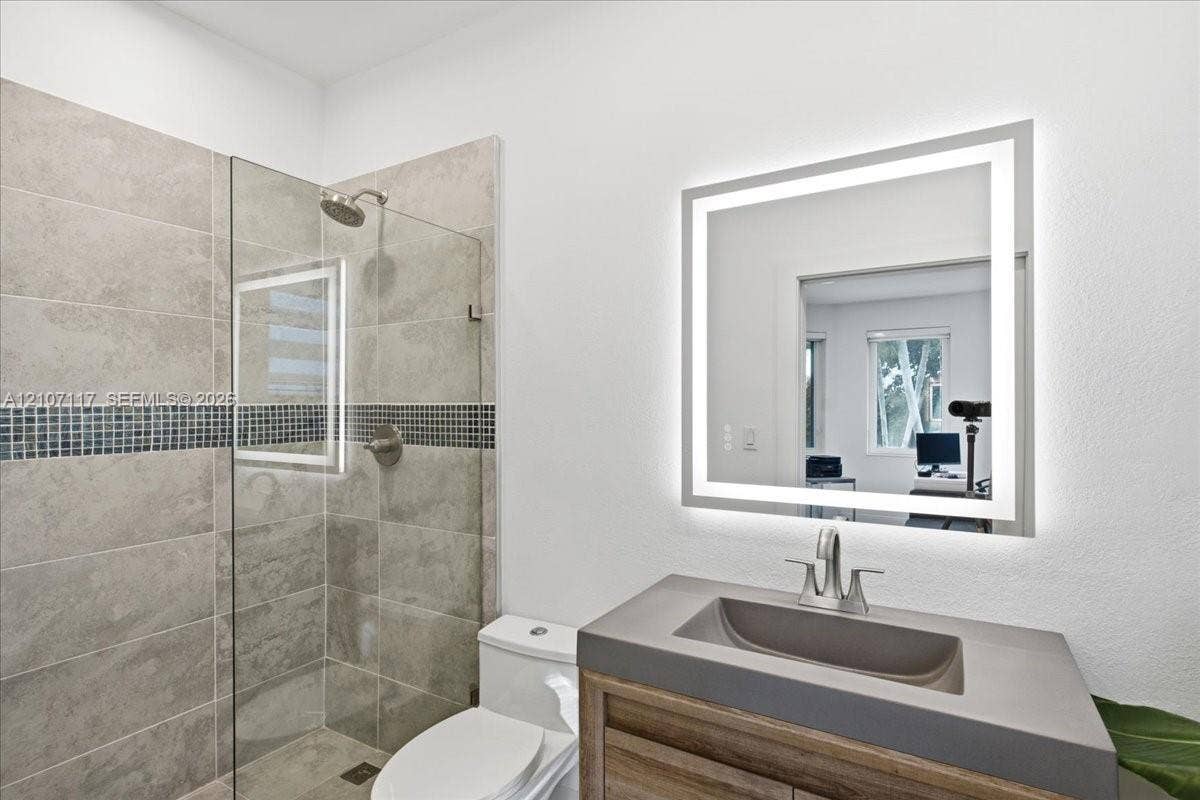7863 NW 111th Court, Doral, FL 33178 Walk-in shower with stone-finish tile and a mosaic tile inlay, wood-finish vanity with a molded sink, and a wall-mounted LED-backlit mirror