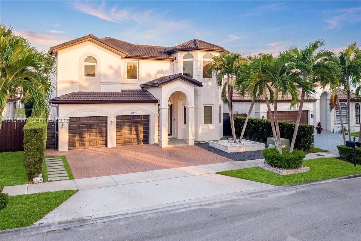 7863 NW 111th Court, Doral, FL 33178 Two-story stucco exterior featuring a covered arched entryway, tiled roof, decorative masonry planter, and a multi-car garage with paneled doors