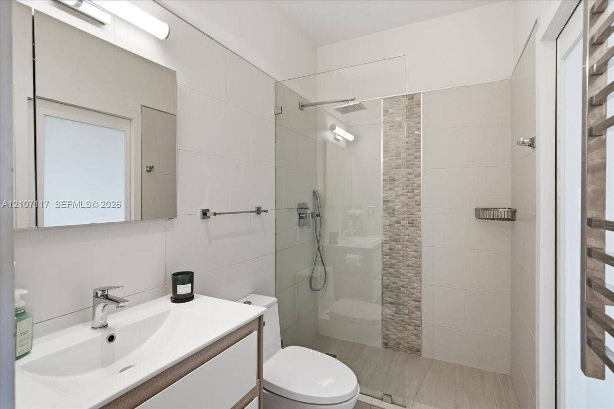 7863 NW 111th Court, Doral, FL 33178 Bathroom featuring a vanity with integrated sink, frameless glass-enclosed shower with tiled decorative inlay, wall-mounted medicine cabinet, and polished chrome fixtures