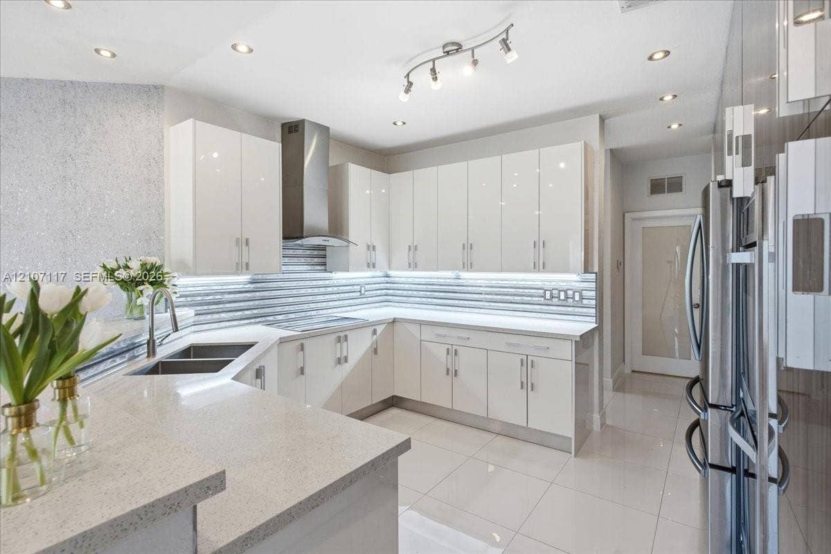 7863 NW 111th Court, Doral, FL 33178 Kitchen featuring high-gloss white cabinetry, quartz countertops, horizontal textured tile backsplash, stainless steel range hood, and large-format porcelain tile flooring