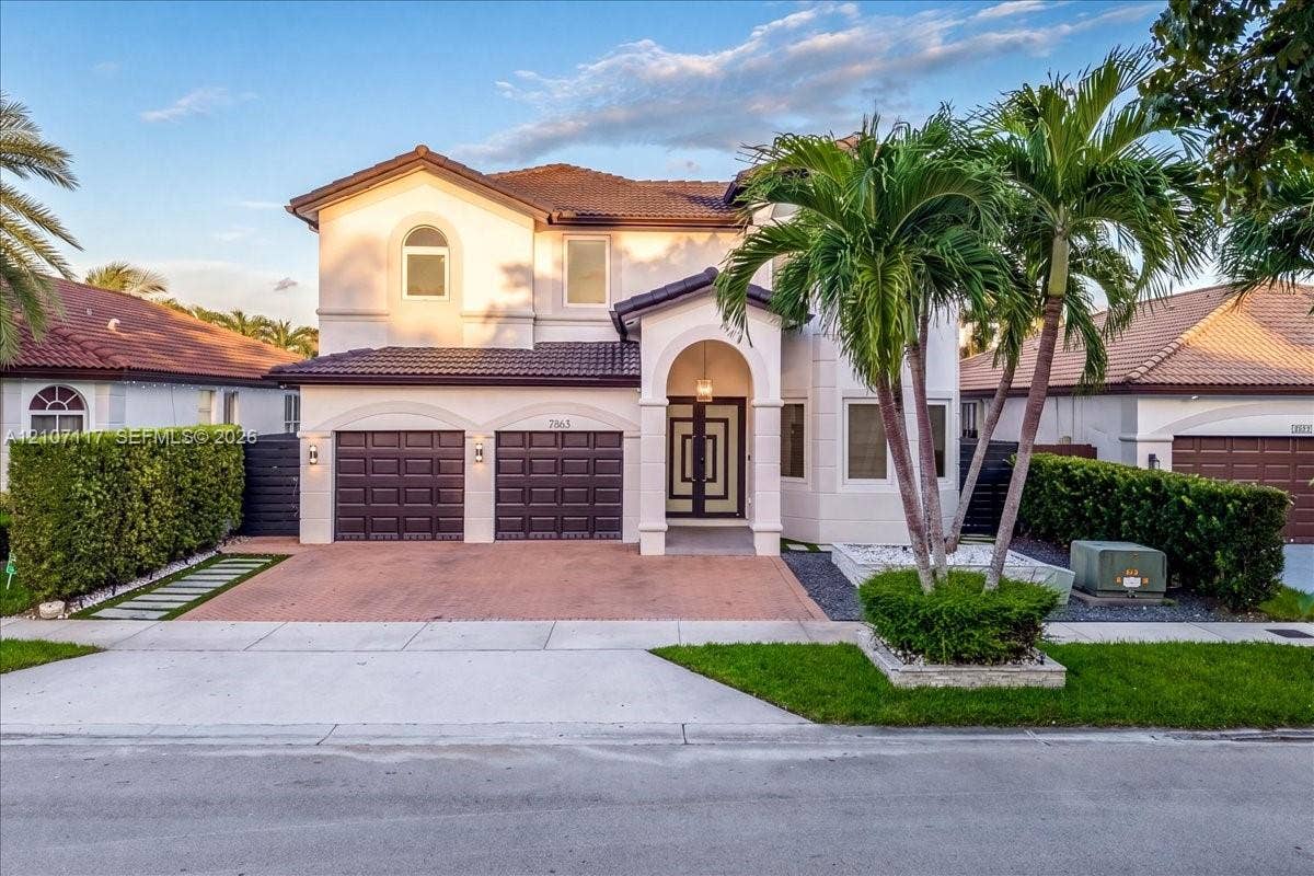 7863 NW 111th Court, Doral, FL 33178 Two-story residence featuring a tile roof, paved driveway, three-car garage, arched covered entryway, and double-entry doors