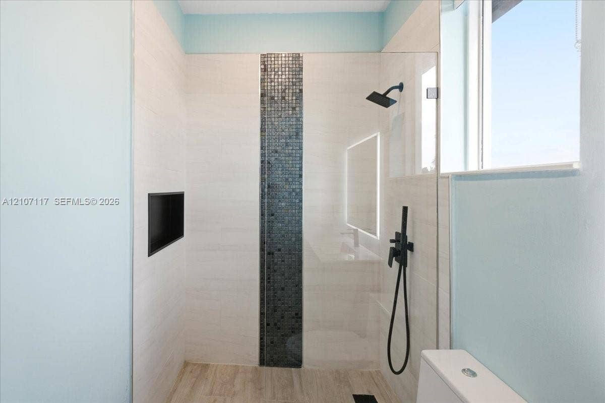7863 NW 111th Court, Doral, FL 33178 Walk-in shower featuring large-format wall tile, a vertical mosaic accent strip, matte black wall-mounted shower hardware, a recessed wall niche, and a glass partition