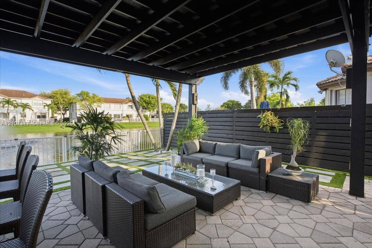 7863 NW 111th Court, Doral, FL 33178 Covered patio featuring a black timber pergola, horizontal privacy fencing, concrete pavers with integrated turf, and water frontage