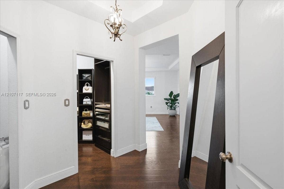7863 NW 111th Court, Doral, FL 33178 Tray ceiling featuring an ornate metal chandelier, dark wood-finish flooring, and a built-in walk-in closet system with dark wood cabinetry