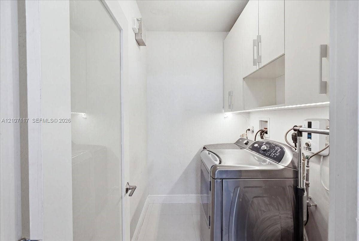 7863 NW 111th Court, Doral, FL 33178 Laundry area featuring flat-panel white cabinetry, under-cabinet task lighting, polished tile flooring, and a solid-core interior door with modern lever hardware