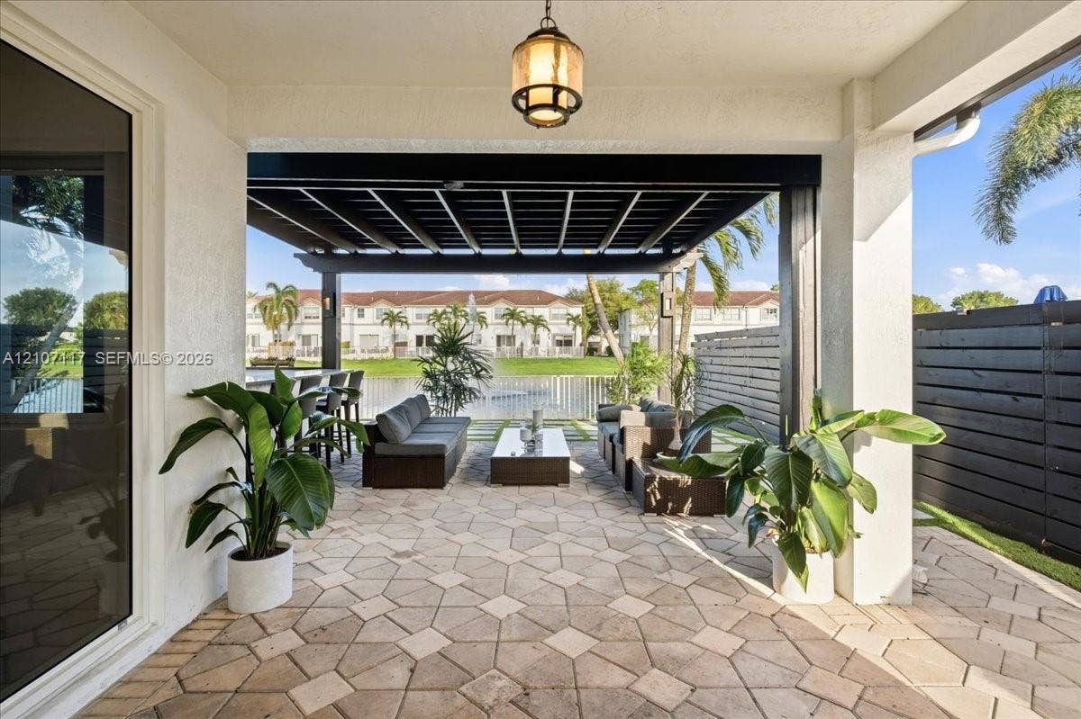 7863 NW 111th Court, Doral, FL 33178 Covered patio featuring patterned stone pavers, a dark wood-finish pergola, recessed ceiling lighting, and a dark horizontal slat privacy wall