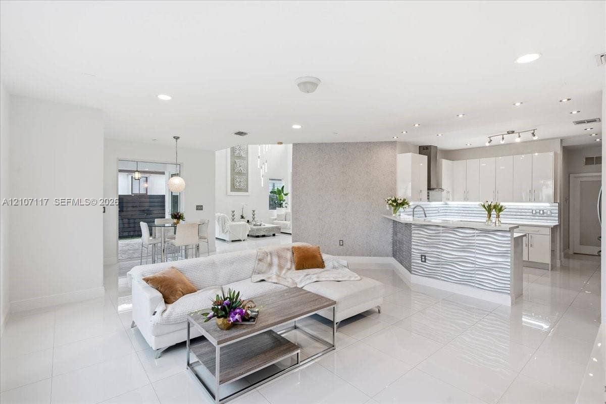 7863 NW 111th Court, Doral, FL 33178 Open-concept interior featuring large-format tile flooring, high-gloss kitchen cabinetry, a textured stone feature wall, and a raised breakfast bar with horizontal wave-patterned paneling
