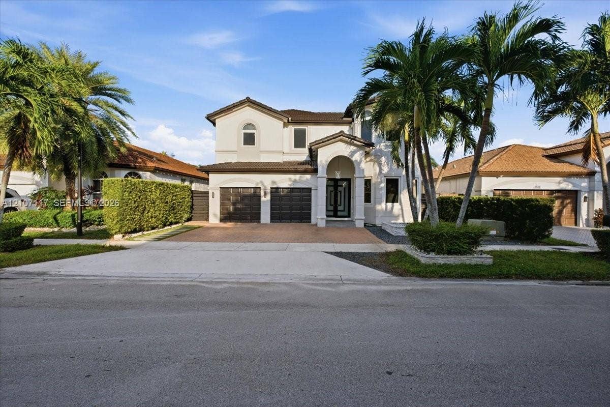 7863 NW 111th Court, Doral, FL 33178 Two-story stucco exterior featuring a tiled roof, arched entryway, paved driveway, and multiple palm trees