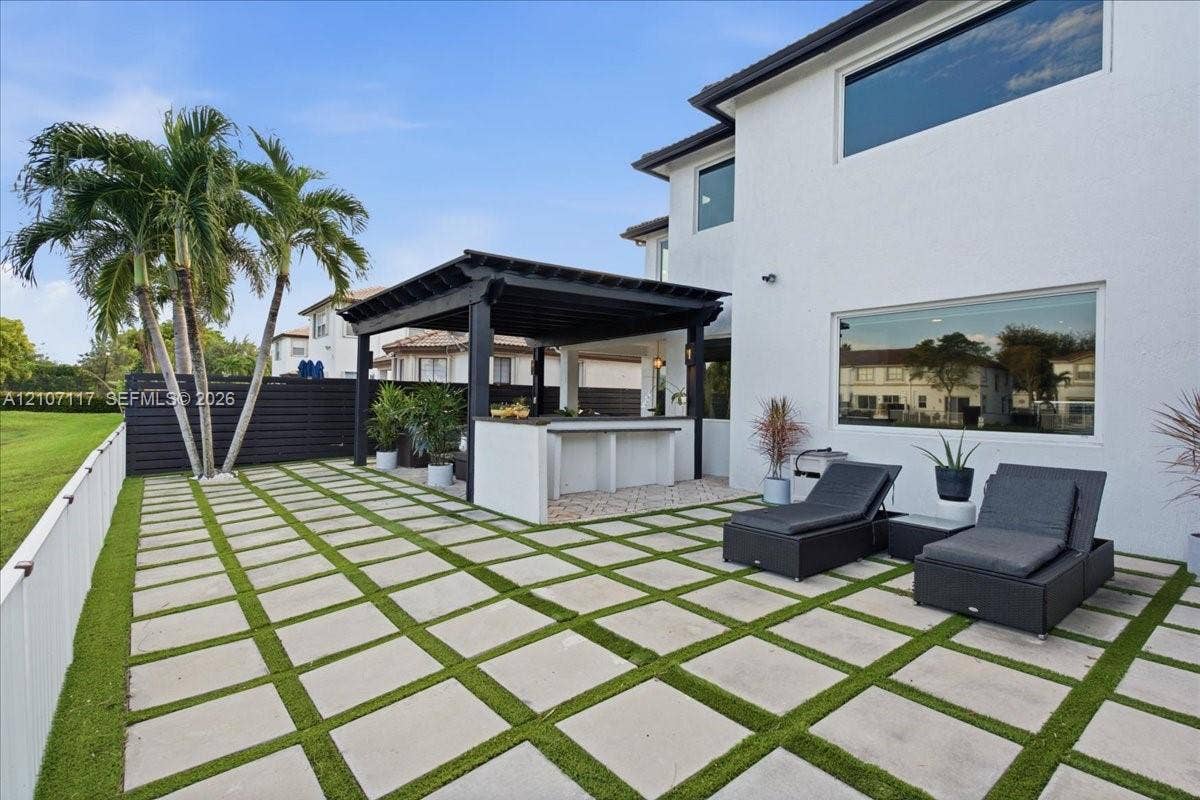 7863 NW 111th Court, Doral, FL 33178 Outdoor living area featuring a covered pergola, integrated bar counter, large-format paver patio with turf inlay, and horizontal slat privacy fencing