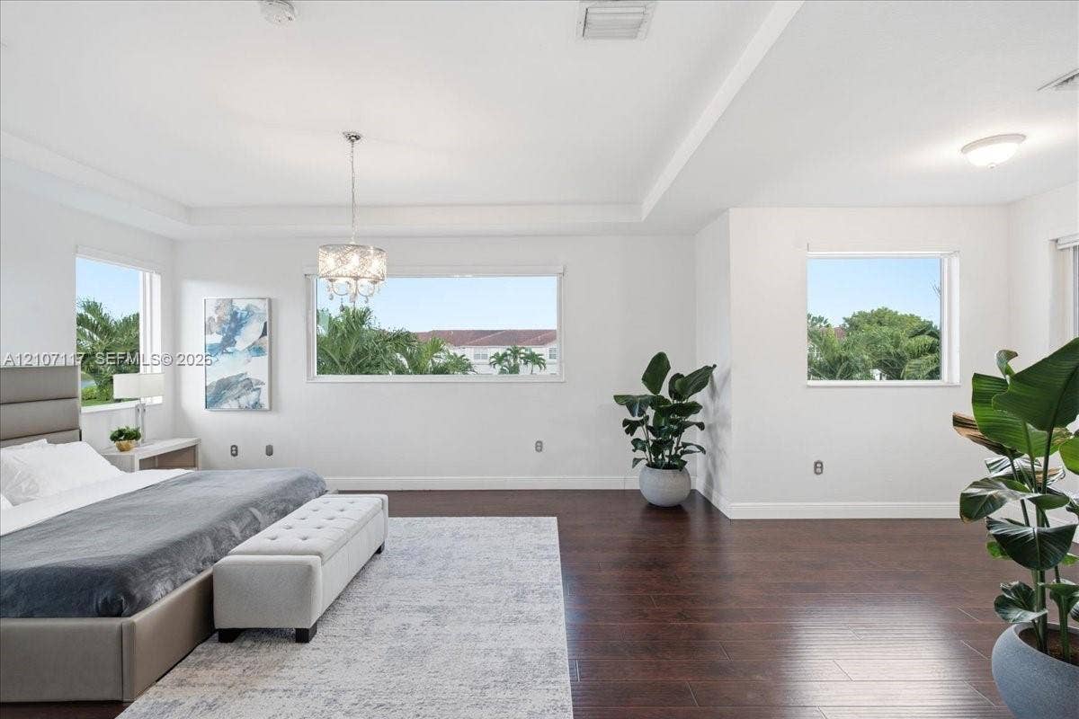 7863 NW 111th Court, Doral, FL 33178 Spacious room featuring wood-finish flooring, recessed ceiling tray detailing, and a multi-tiered crystal chandelier