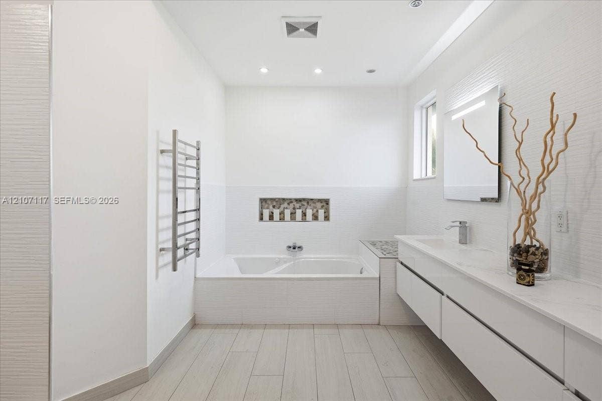 7863 NW 111th Court, Doral, FL 33178 Floating double vanity with quartz countertop, inset soaking tub featuring a decorative stone mosaic niche, wood-finish tile flooring, and wall-mounted heated towel rack