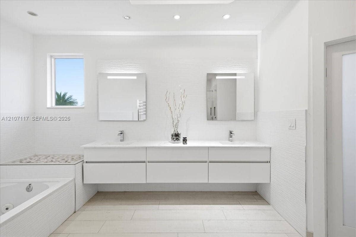 7863 NW 111th Court, Doral, FL 33178 Floating white double vanity with polished stone countertop, rectangular undermount sinks, wall-mounted light fixtures, tiled bathtub surround with stone inlay, and tile flooring